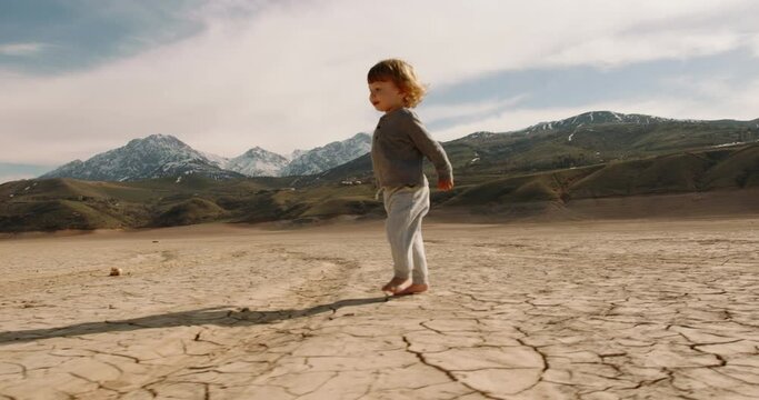 Funny caucasian baby boy running on deserted ground. Cracked soil land after erosions and desertification - ecology, save our planet concept 4k footage