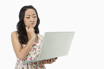Woman using a laptop while standing, contemplating