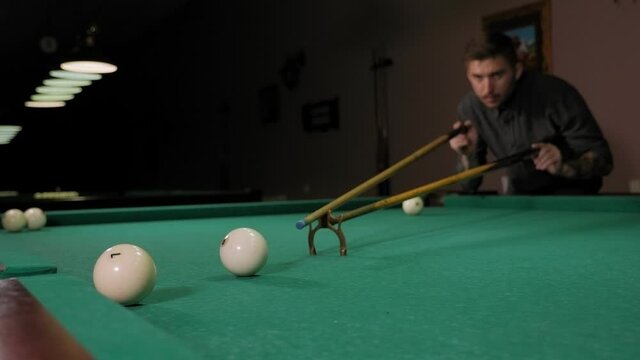 Close-up of a man playing pool in a dark bar, he hits the ball with a cue and hits the hole. Playing Billiards on the green table.