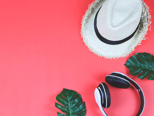 Music , travel and relaxation concept.Top view or flat lay of headphones, hat and tropical monstera leaves on red background