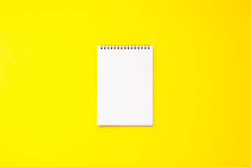 a blank white flipchart of a notebook on a spring on a bright yellow background.