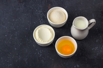 Baking background. Ingredients for cooking cake (flour, egg, sugar, milk) in bowls on dark table. Food concept. Close up layout, copy space for text.