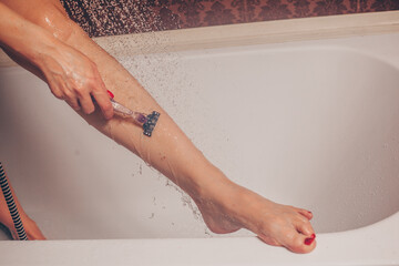 Close up of woman shaving legs in bathroom.