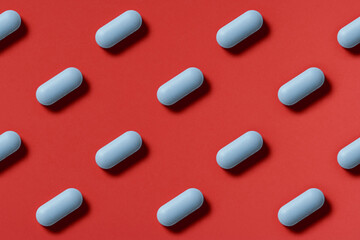 medicine, healthcare and pharmacy concept - blue pills or capsules lie in rows diagonal on red background top view copy space pattern