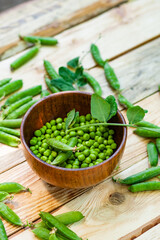 closeup green peas in brown dish, on wooden table.