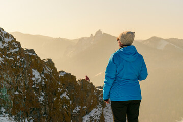 A woman in the mountains admires peak. View from the back. White snow on rocks, fog in valley, the sun's rays. Concept of tourism, achieving the goal.
