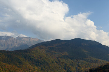 nature landscape and travel concept - mountains and trees against the blue sky with clouds in early autumn
