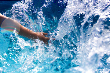 Hand in blue water close-up. The child splashes in the water. Spray and drops in the sun. Glare of light. Swimming in the pool.