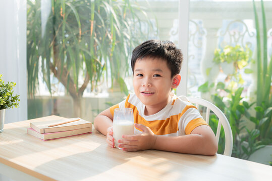 Adorable happy young Asian boy having breakfast and drinking milk at home in the morning; looking at camera