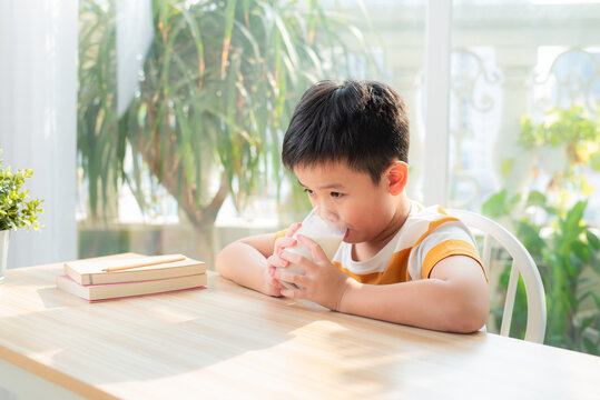 Cute boy drinking glass of milk sitting at a table after doing the homework