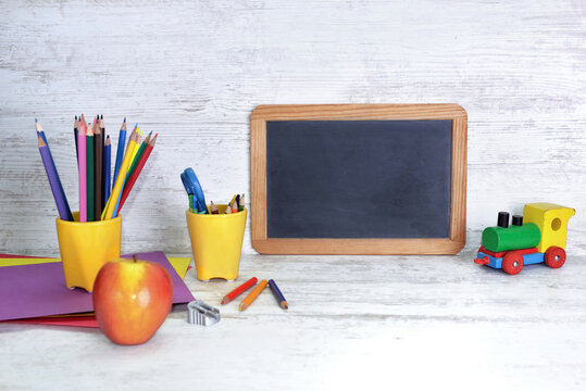 black board on a kid desk with colorful pencils in yellow pot and toy abd apple