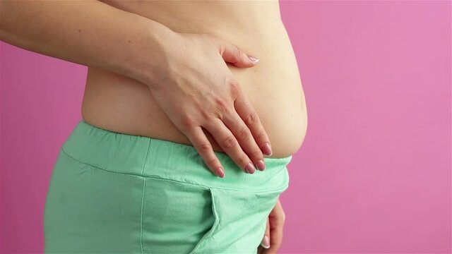 obese woman tucking her big belly in. side view pink background close up