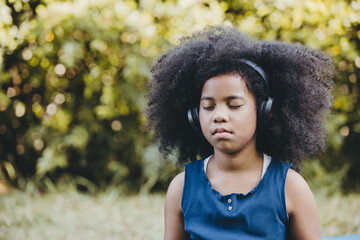 Black african girl children using headphones listening music eyes closed focus and concentrate at green park outdoor