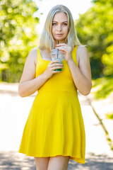 Blonde woman in short yellow dress drinking coctail in park