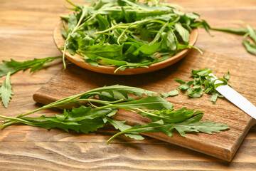 Plate with fresh arugula and cutting board on wooden background
