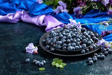 Summer still life with blueberries, colored sweet peas and meadow grasses on a dark blue table.
