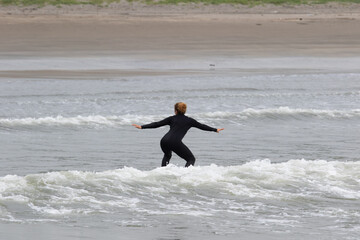 Young multiracial African American lady with amazing smile, freckles & frizzy hair, learning to surf wearing a black wetsuit on a black surfboard. She is Surfing in Chiba Japan near to Ichinomiya.