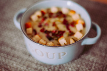 Zuppa soup di patate, con scalogno, erba cipollina, prezzemolo, pezzetti di prosciutto crudo e crostini di pane in una ciotola mono porzione in ceramica