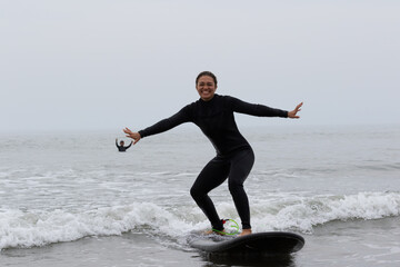 Young multiracial African American lady with amazing smile, freckles & frizzy hair & an Asian Japanese Surf Instructor having a surf lesson together in Chiba, Japan They are wearing black wetsuits.