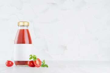 Fresh red tomato juice in glass bottle with blank label template with green parsley, vegetables slices on wood table and white background with copy space.