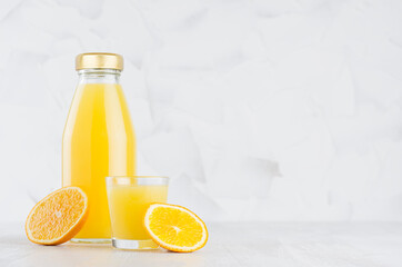 Bright fresh orange juice in glass bottle template with wine glass decorated  fruit slices in soft light white interior on wood table with copy space.