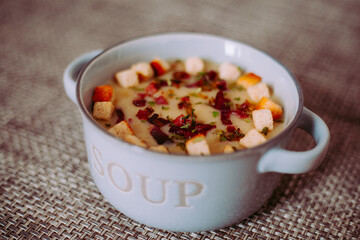Zuppa soup di patate, con scalogno, erba cipollina, prezzemolo, pezzetti di prosciutto crudo e crostini di pane in una ciotola mono porzione in ceramica