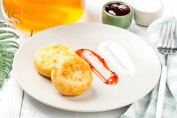 Two cottage cheese pancakes on a white plate with sour cream and jam for breakfast