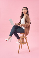 Beautiful and happy woman working with a laptop, isolated over pink background