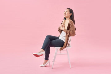 Young woman with book sitting on chair over pink