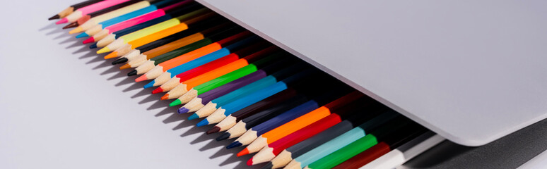 Obraz premium colored pencils in modern laptop on white background, panoramic shot