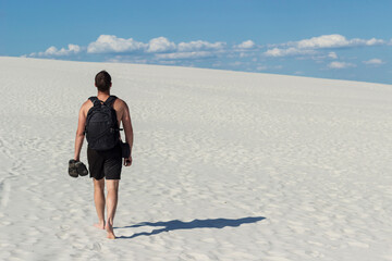 man with a backpack walks alone on the sand in the desert, sunny weather