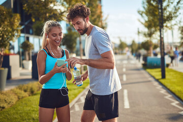 Modern couple making pause on the sidewalk during jogging / exercise.