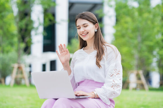ノートパソコンの画面に向かって手を振る若い女性