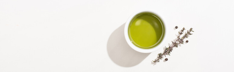 top view of olive oil in bowl near herb and black pepper on white background, panoramic orientation