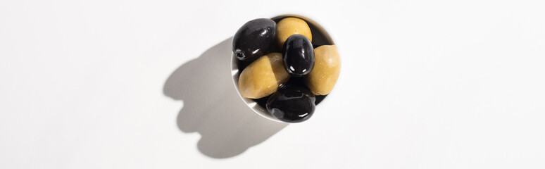 top view of black and green olives in bowl on white background, panoramic orientation