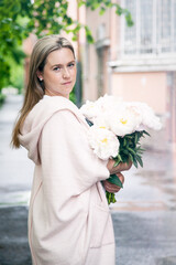 A woman with a bouquet of peonies walks along the street