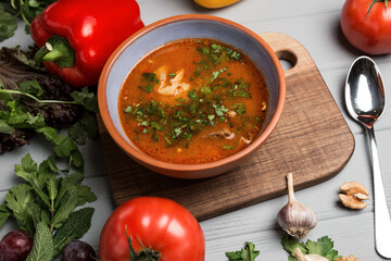 a plate of borsch with a spoon and a hand. chilli scattered around. gray wooden background