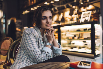 Contemplative female millennial in electronic headphones listening music podcast during leisure time for resting, thoughtful hipster girl in earphones pondering on plot of interesting audio book