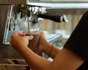 Close up barista female hands with a transparent glass cup in hands pouring coffee from a coffee...