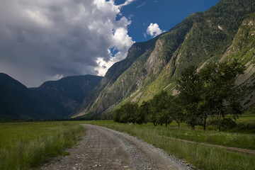 stone road in a mountain gorge, high mountains, tourist summer landscape with white clouds in the blue sky,