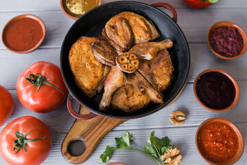 Grilled meat. Baked chicken in a pan close-up. Gray wooden background, spicy sauces and cutlery. Georgian cuisine