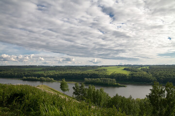 view of the river from a high mountain, summer landscape of deciduous forest, the sun shines through the clouds, a landscape of moderate temperate climate