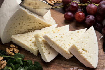 Slices of triangular cheese on a board. There are a lot of vegetables and grapes around. close-up top view. Georgian cuisine