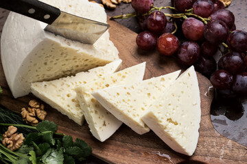 Slices of triangular cheese on a board. There are a lot of vegetables and grapes around. close-up top view. Georgian cuisine
