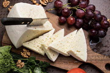 Slices of triangular cheese on a board. There are a lot of vegetables and grapes around. close-up top view. Georgian cuisine