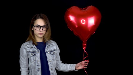 A sad woman stands with helium balls on a black background. Valentine's Day is the day of all lovers.