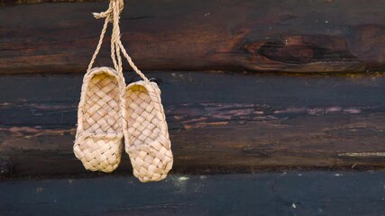Antique handmade rustic shoes - bast shoes. A pair of bast shoes hanging on the background of a wooden log wall.