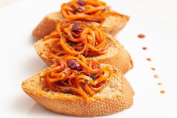 Croutons of bread with caramelized carrots and onion on a white plate 