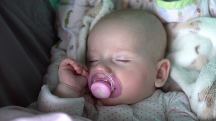 A baby is sleeping with a pacifier in its mouth in a stroller. Face close up.