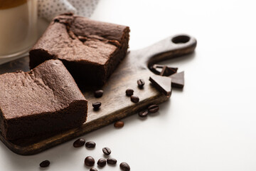delicious brownie pieces on wooden cutting board with coffee beans and chocolate on white background